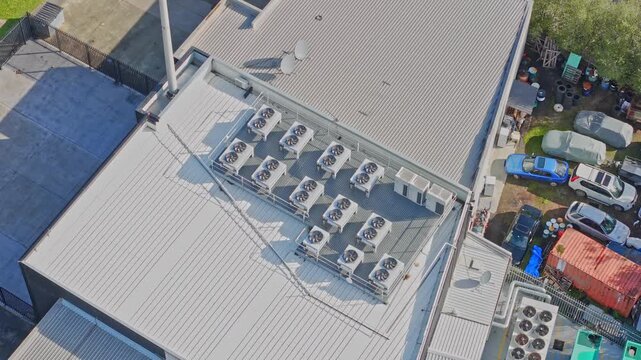 Drone shot captures a data centre rooftop with industrial HVAC units, metallic surfaces, and a fleet of servers below in bright daylight. Clean geometric lines, clear sky, no people present.