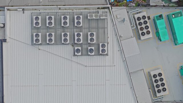 Cinematic aerial footage of a large data center rooftop reveals arrayed HVAC cooling fans, metallic surfaces, and industrial geometry in daylight. No people visible. Static overhead shot.