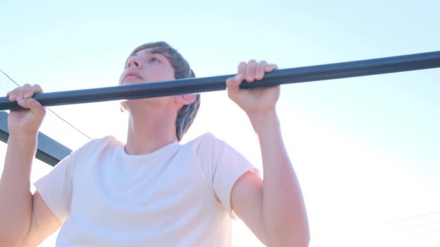 Teenage athlete performs pull ups on a horizontal bar at an outdoor workout park. Calisthenics training, self discipline, endurance, strength development and healthy lifestyle.