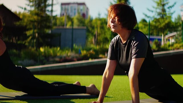 Elderly women practicing slow motion Pilates outdoors on yoga mats, performing gentle back extension exercises for strength, flexibility, and healthy aging together