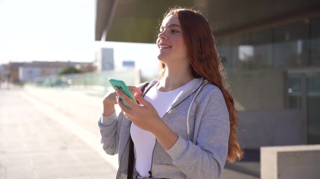 A cheerful teenage girl is engaging happily with her smartphone while outdoors during the day