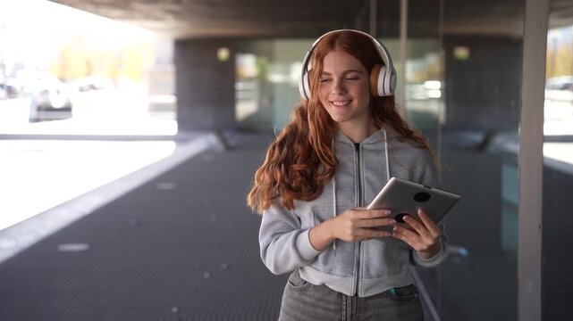 A young woman enjoys music through her tablet and headphones outdoors in a lively city