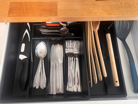 Open kitchen drawer with cutlery organizer. Silverware and utensils stored in a tray.
