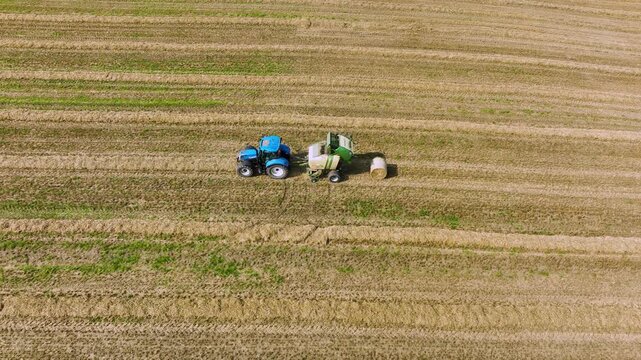 Aerial View of Tractor Pulling Round Baler Across Golden Field with Fresh Hay Bale
