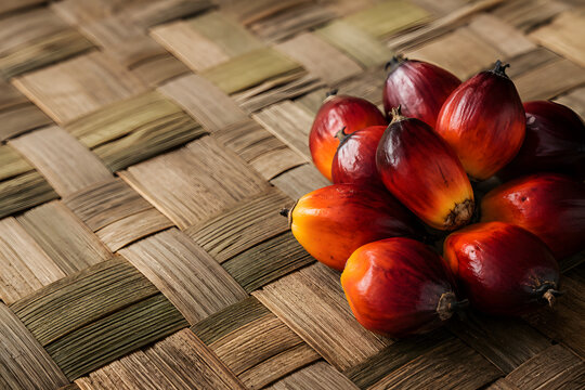 Fresh raw palm oil fruitlets displaying vibrant red and orange gradient skins on woven pandan mat