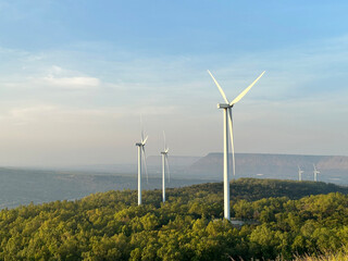 Large wind turbines rising above lush green forest canopy © kritaya