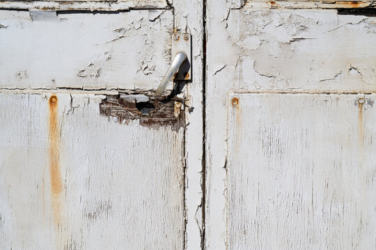 Weathered white wooden doors with peeling paint, rust stains and worn metal door handle