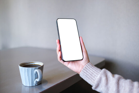 Mockup image of a woman holding mobile phone with blank desktop screen