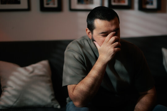 Sad Man Making Facepalm Gesture Sitting Worried On Couch. Disappointed stressed male covers his eyes while leaning forward on a sofa
  