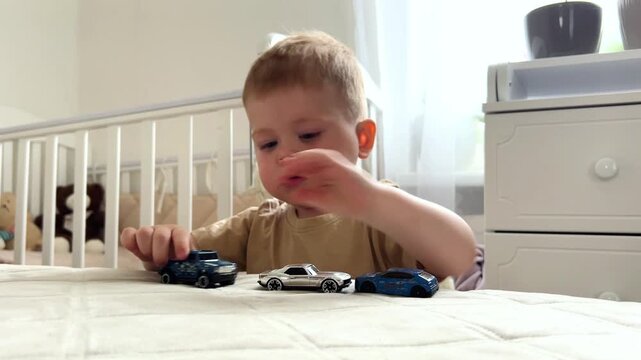 Two year old boy playing with small cars on bed. Racing and parking toy vehicles. Fine motor skills through push and go play. Classic boyish toy fun