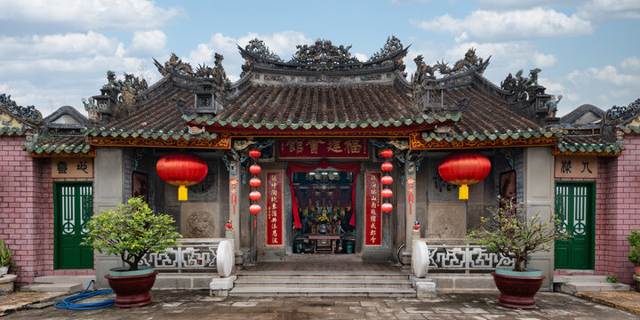 Hoi An, Vietnam - May 1, 2026: Traditional architecture of the historic Phuc Kien Assembly Hall featuring ornate roof details, hanging red lanterns, and bonsai trees in the ancient town of Hoi An