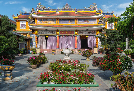 Exterior view of the Phap Bao Pagoda or Chua Phap Bao with traditional architecture and vibrant flower beds in the courtyard in the historic city of Hoi An, Vietnam