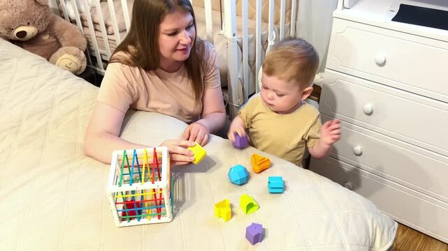 Mother and two year old son playing with colorful cubes. Parent child play teaches size order and logic. Fine motor skills development through classic toy