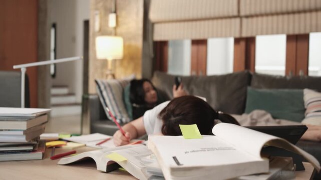 Two College Asian friends, teenage girl tired and burned out from overwhelmed homeschooling, study pile of books, stressed learning at home, her friend wakes up while napping, education exam support.