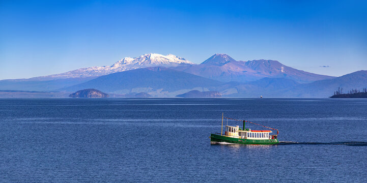 Lake Taupō, New Zealand. Snowy volcanoes Mt Ruapehu, Ngauruhoe and Tongariro. Tourists on replica steam boat in foreground. Panoramic view. Volcanic activity at Ketetahi Springs, Mt Tongariro.
