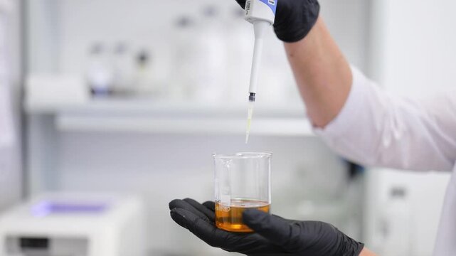 Laboratory professional carefully dispenses liquid into beaker. Scientific research and development in pristine, modern lab. Precision work with chemicals for pharmaceutical, cosmetic, medical testing
