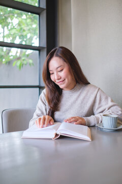Vertical portrait image of a woman reading a book with coffee cup on the table