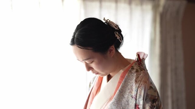 Soft light illuminates a woman in traditional attire. She gazes downward, expression calm and thoughtful. Her hair is neatly styled with a delicate accessory