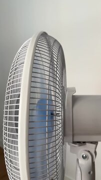 A running white pedestal fan oscillates toward the viewer as the camera pans right to left. Electric fan at home