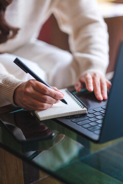Vertical closeup image of a woman writing on a notebook while working on laptop computer