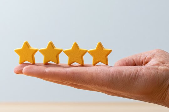 Hand holds four yellow stars against a soft grey backdrop