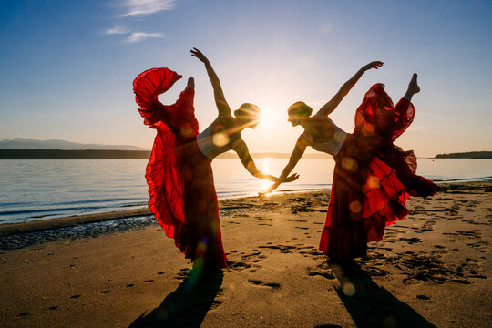 Two white women doing partner acrobatics yoga on a beach at sunset