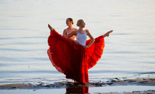 Two white women practice partner acrobatics on a beach at sunset