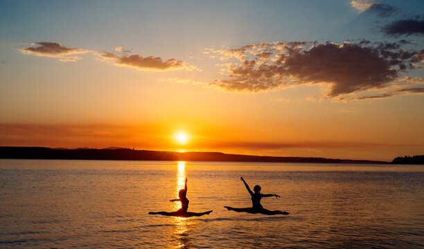 Two white people performing jumping split poses at sunset on a lake