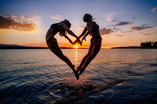 Two white women jump and practice partner acrobatics yoga together
