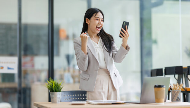 Businesswoman celebrating success and achieving goals, receiving good news on smartphone in modern office
