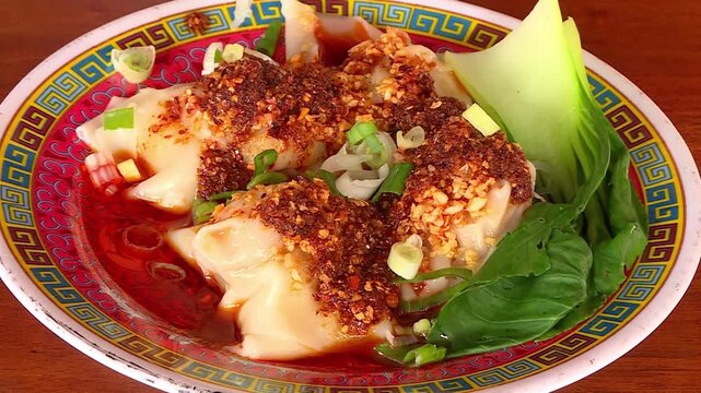 Close-up shot of dumplings coated in chili oil on a plate with pak choi and green onion. The vibrant spicy sauce and fresh garnishes create a delicious, appetizing food presentation. 