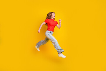 Fototapeta premium Young woman jumping joyfully against a yellow background in casual red shirt and jeans, energetic lifestyle and freedom expression