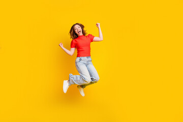 Fototapeta premium Happy young woman jumping in casual jeans and red top against bright yellow background celebrating joy and energy