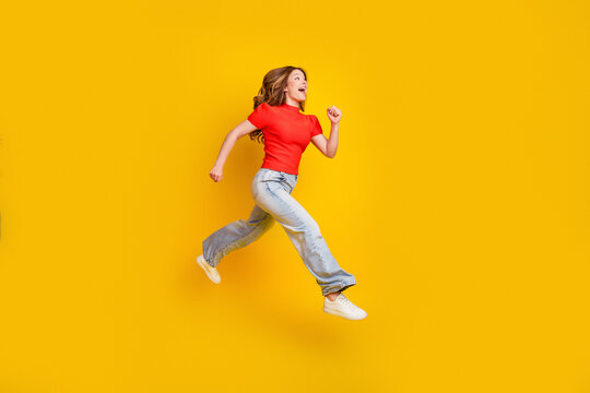 Young woman jumping joyfully against a yellow background in casual red shirt and jeans, energetic lifestyle and freedom expression