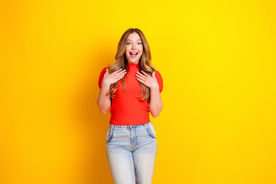 Surprised happy young woman in red top standing against bright yellow background expressing excitement and joy
