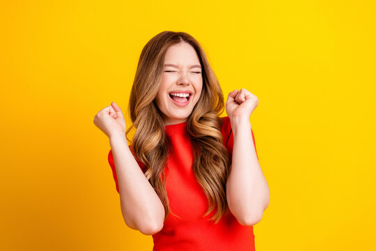 Happy excited woman celebrating with fists raised in bright studio against yellow background, smiling and energetic portrait conveying joy, success, enthusiasm and positive lifestyle vibes