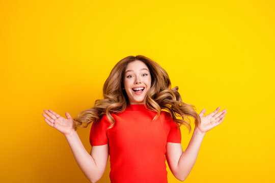Happy young woman with surprised smile and open arms wearing red top on bright yellow background, energetic joyful expression for celebration, lifestyle and positive emotions concept
