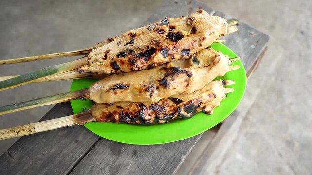 Close-up shot of grilled milkfish satay perfectly charred on bamboo skewers. The traditional minced seafood presentation showcases a savory texture and authentic culinary craft. 
