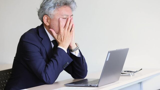 ノートパソコンの前で顔を覆い悩む中高年の男性ビジネスマン