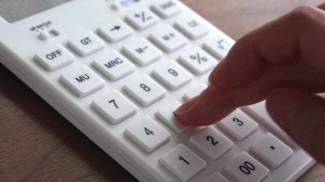 木製テーブルに置いた白い電卓で計算している女性の指先のクローズアップ