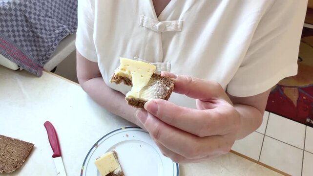 A close-up shows the upper body of a woman enjoying a homemade cheese sandwich prepared with butter and whole grain bread. Static close-up from above