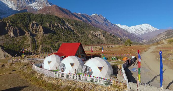 Annapurna Circuit, Manang Nepal, pull out drone shot of luxury geodesic glamping dome tents nestled in an alpine valley beneath a snow-capped mountain range in morning light.