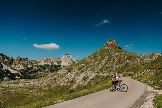 Female cyclist with gravel bike stopping on the mountain road at Sedlo Pass in Durmitor National Park, Montenegro. Stunning alpine scenery surrounds the scenic cycling route