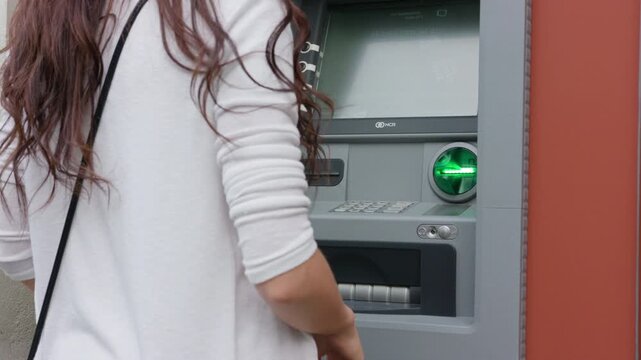 Dark haired young woman standing in front of ATM machine preparing to insert her card for secure banking transaction in 4K Ultra HD footage

