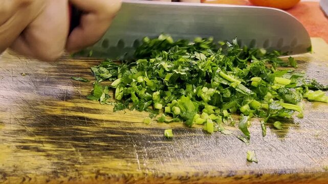 Close up of chopping fresh cilantro with a chef knife on a wooden cutting board during preparation of homemade tuna ceviche in the kitchen