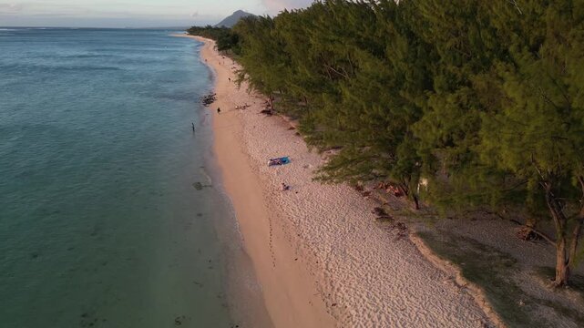 Aerial drone tracking view along the sandy coastline and palm trees of Flic en Flac Beach with distant mountains in Mauritius.