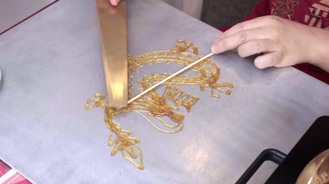An artisan inserts a bamboo stick into a completed sugar dragon, the final tanghua step before serving it as a street treat, Thailand. Part 6 of 6 &mdash; a tanghua sugar dragon created from start to finish