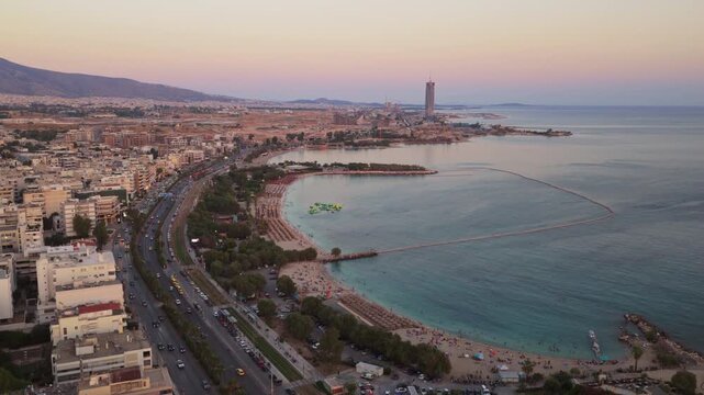 Aerial perspective of the beautiful patras coastline in greece, showcasing the urban landscape with busy streets, a sandy beach, and the calm sea waters during a colorful twilight evening