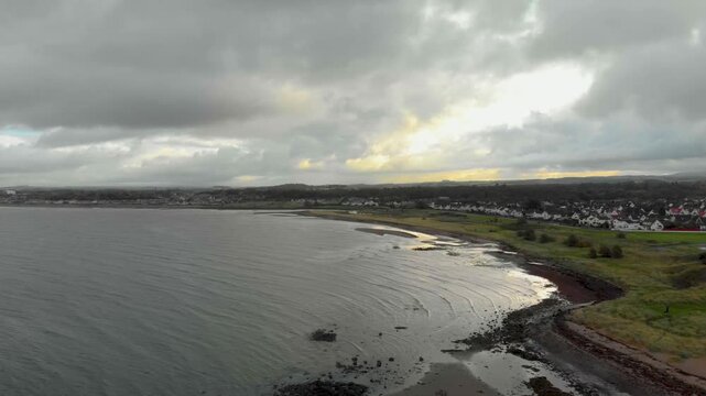 Tracking shot along Greenan Shore coastline under a dramatic cloudy sky, Ayr.