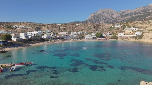 Drone pullback revealing Lefkos Beach in Karpathos, with crystal-clear waters, golden shoreline, and the island's rugged rocky landscape unfolding in the background.